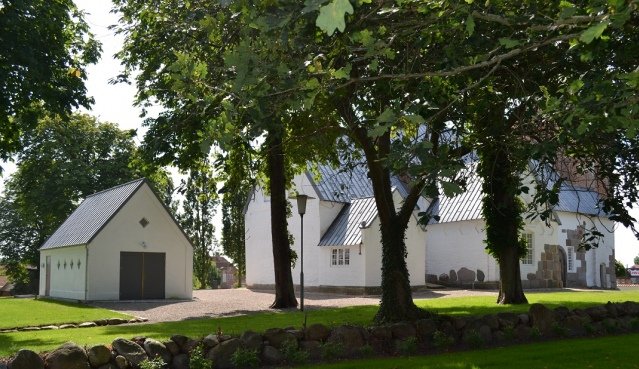 Billede af hvid bygning og garage omgivet af græs og træer.